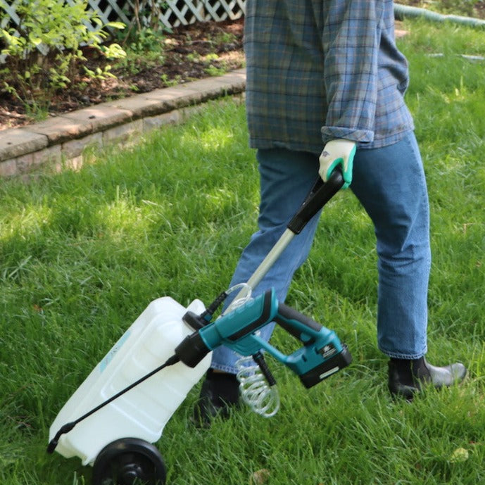 woman pulling rolling trolley sprayer through grass