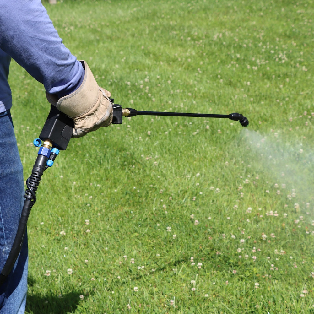 Hand using spray wand to water grass